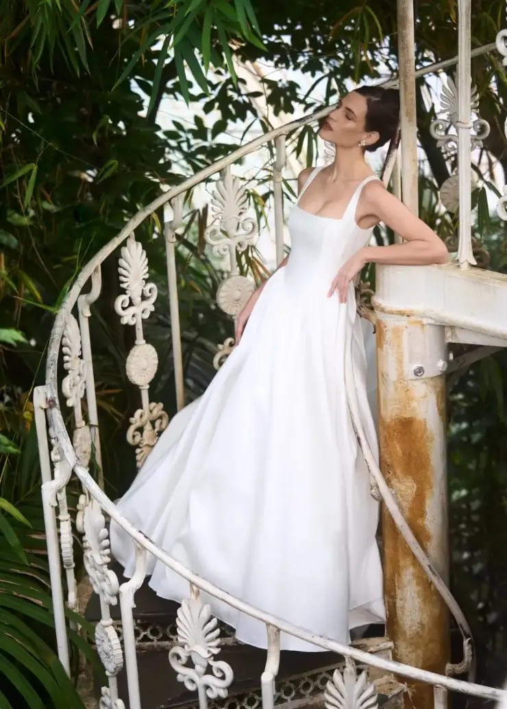 Model is wearing a ball gown wedding dress with a square neckline, drop waist, and sleeveless by caroline castigliano 