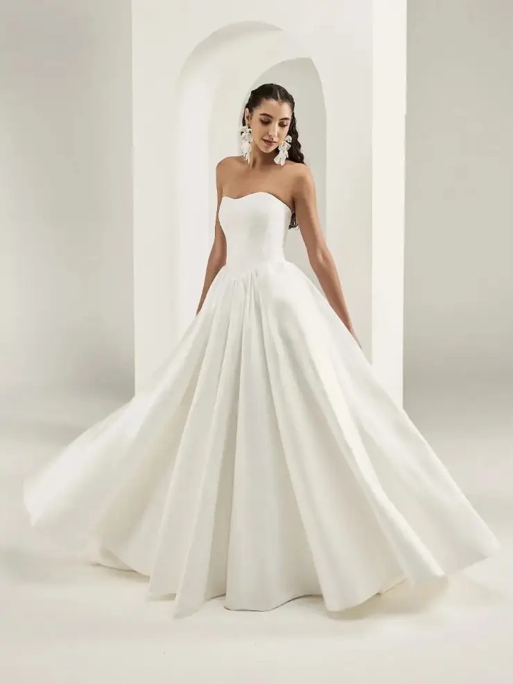 Model is wearing a strapless ball gown wedding dress with a dropped waist and full skirt by savin london