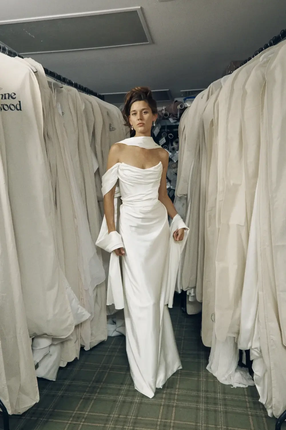 A woman wearing a white gown stands amidst rows of hanging garments.