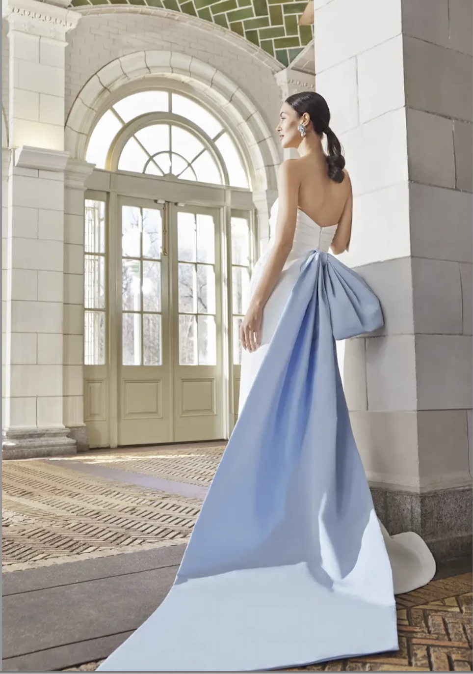 Model is wearing a silk slim flare wedding dress with a blue oversized bow in the back