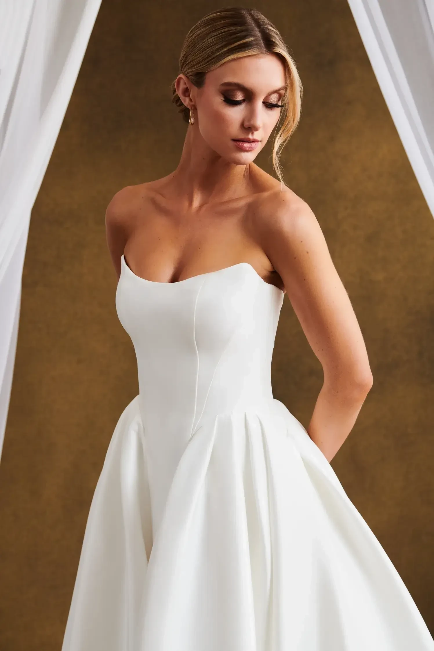 Model is wearing a Mikado ball gown with a scooped neckline, curved basque waist, pleated skirt, and covered buttons.