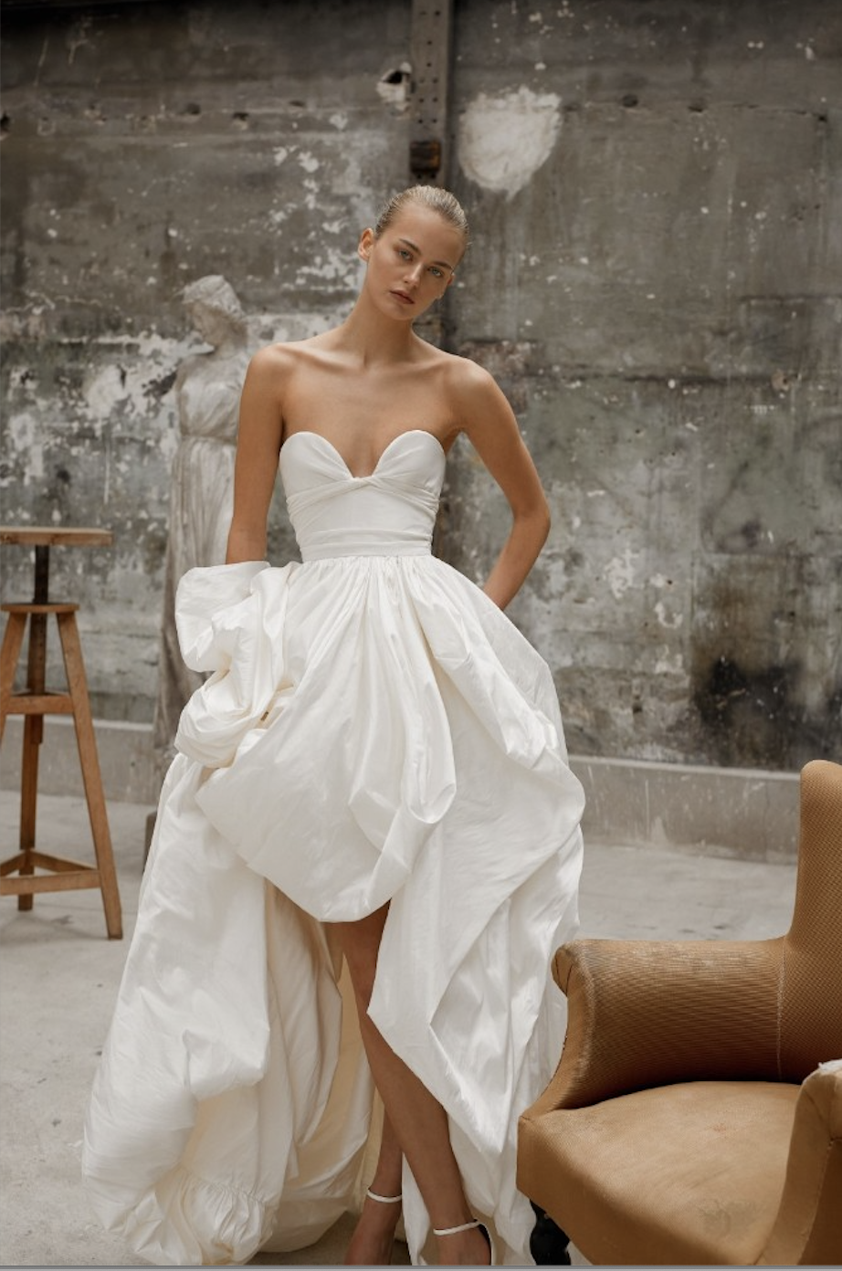 model is wearing a strapless wedding dress by dana harel with a full skirt and structured bodice